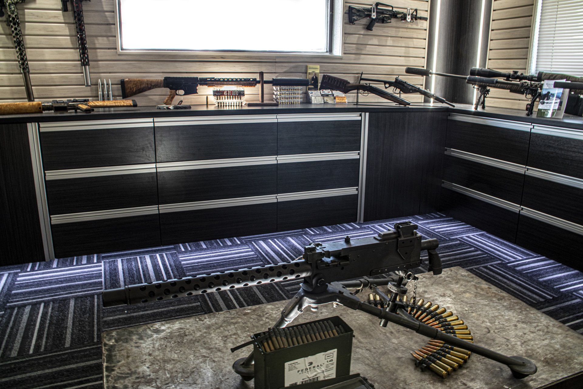 Inside a gun store, machine gun on display with ammunition. Rifles and handguns visible on shelves and counters.