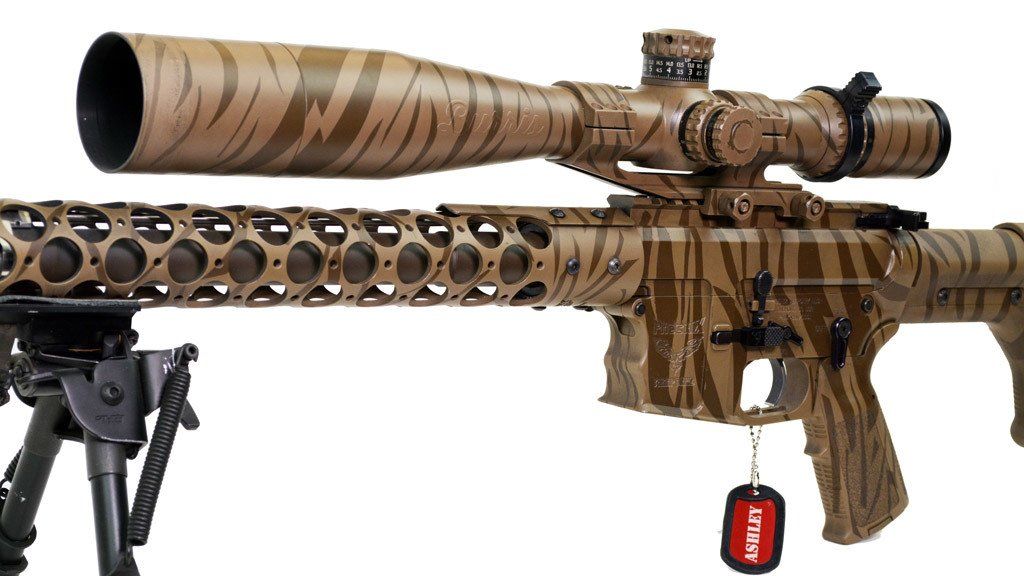 Camouflaged rifle with scope, mounted on a bipod. Brown and tan tiger-stripe pattern.