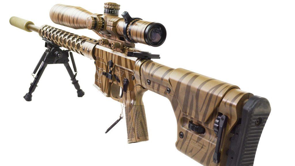 Sniper rifle with camouflage pattern, mounted with a scope and bipod on a white background.
