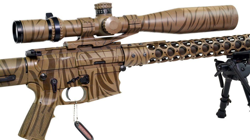Brown and tan camouflage rifle with scope, mounted on a bipod.