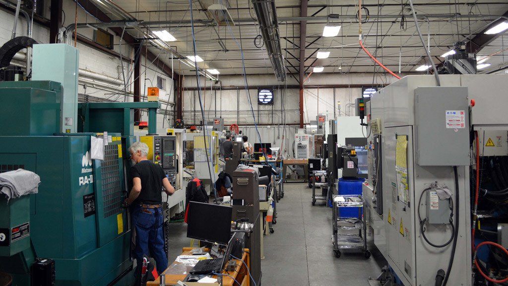 Inside a machine shop; workers operate machinery. Green and gray machines dominate the view.
