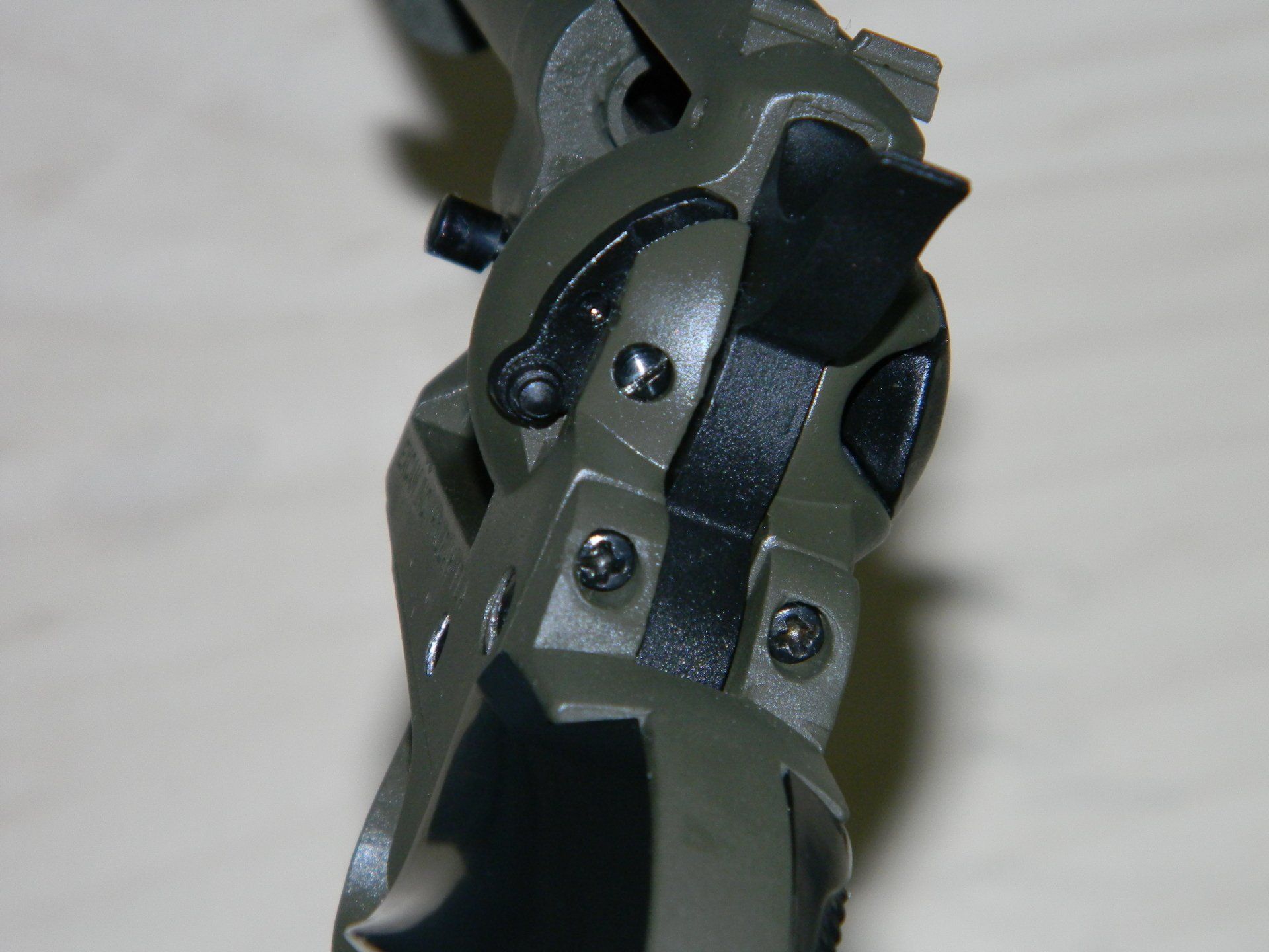 Close-up of a pistol grip. Black and dark green with screws and a small lever visible.