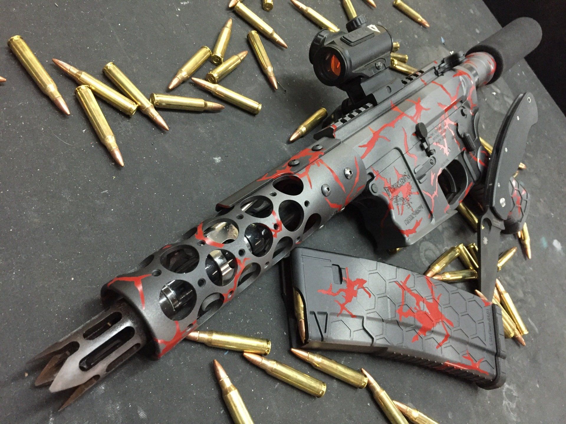 Custom AR-15 rifle with red and black paint, surrounded by brass bullets.