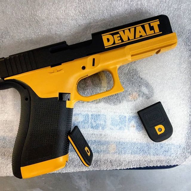 Black and yellow pistol customized with the DeWalt logo, on a white surface with magazine parts nearby.