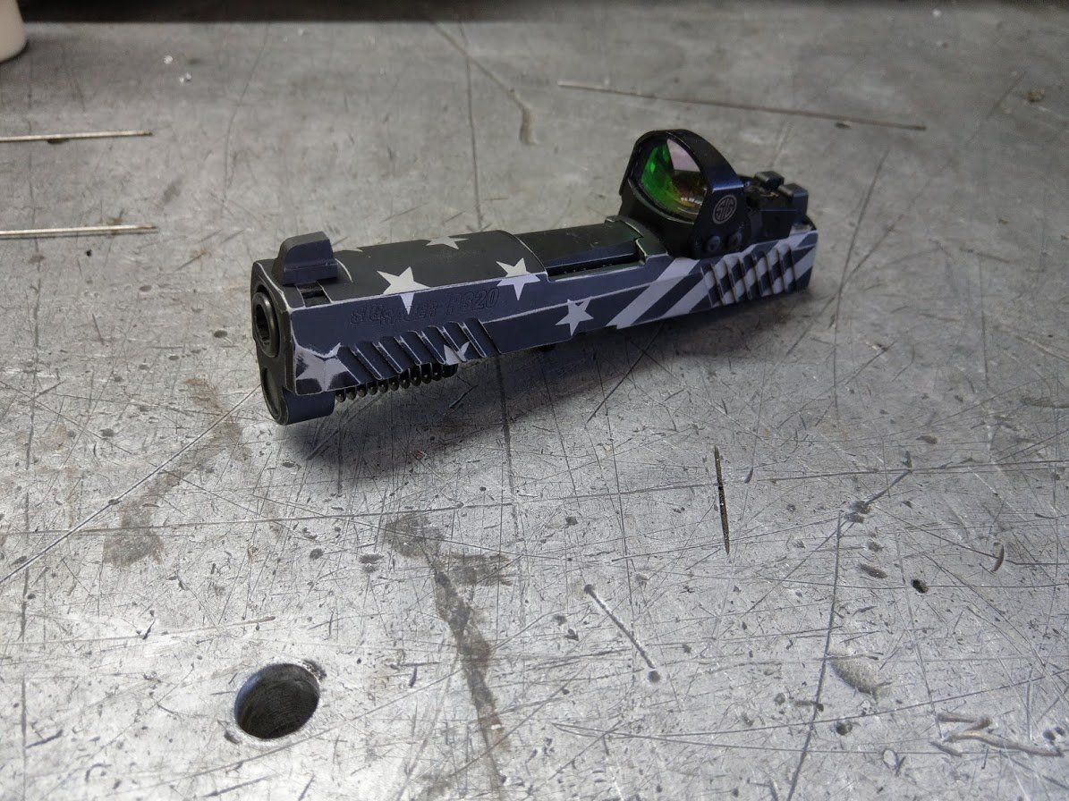 Custom pistol with American flag design and red dot sight on a metal surface.