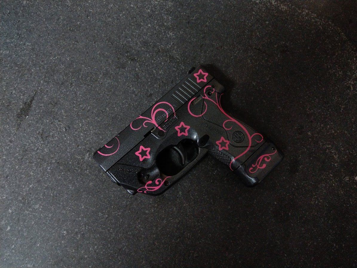 Black handgun decorated with pink stars and swirls on a dark surface.