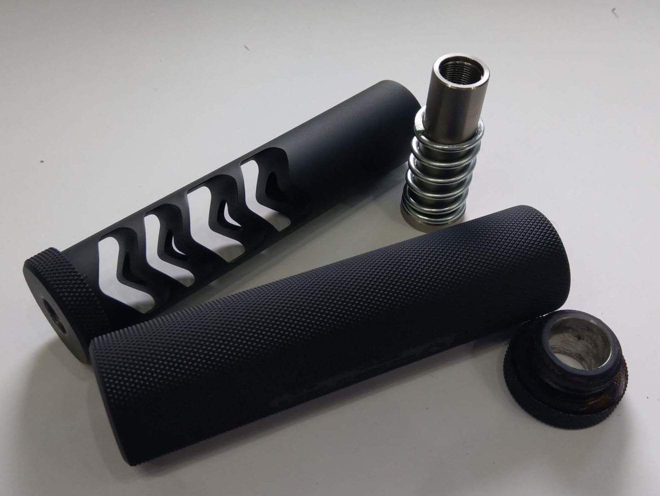 Black rifle accessories: a muzzle brake, handguard, spring, and end cap on a white surface.