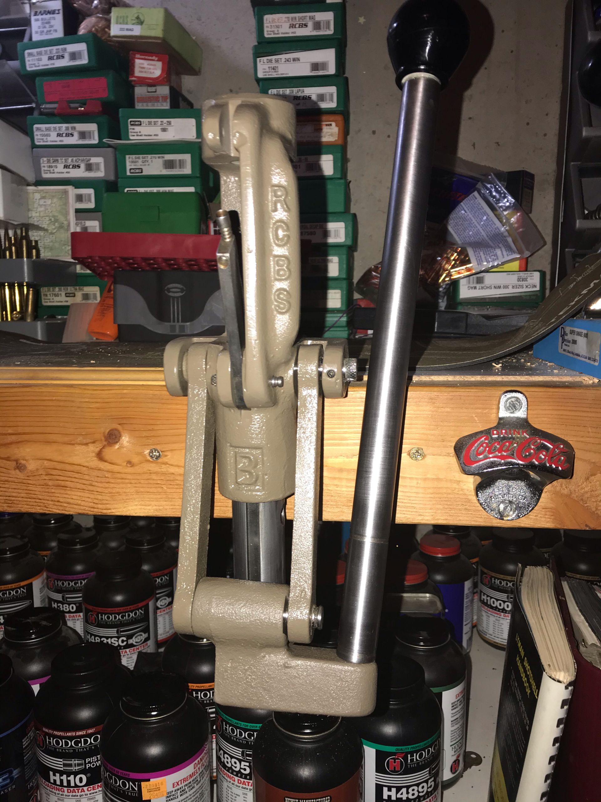 Reloading press with a lever, beige and silver, sitting in front of containers.