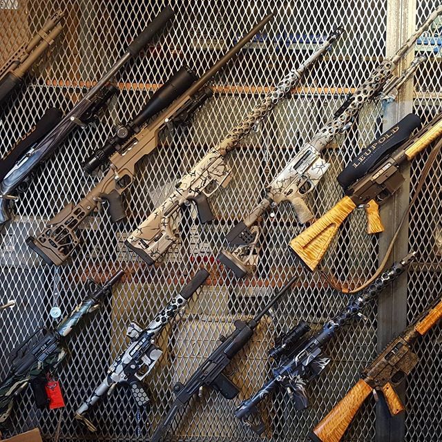 Assortment of rifles, various designs and camouflage patterns, mounted on a metal grid background.