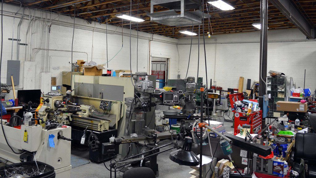 Workshop with various machinery, tools, and equipment, lit by overhead fluorescent lights.