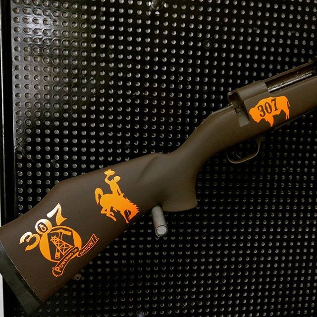 Brown rifle with orange Wyoming-themed decals, including