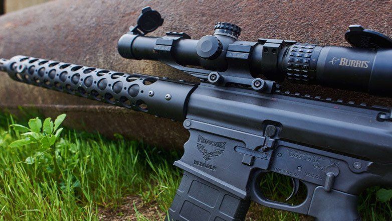 Black rifle with scope on grass, barrel with vents.