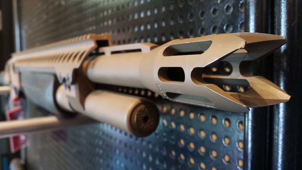 Tan shotgun muzzle with vents and a cylinder mounted underneath, against a black background.
