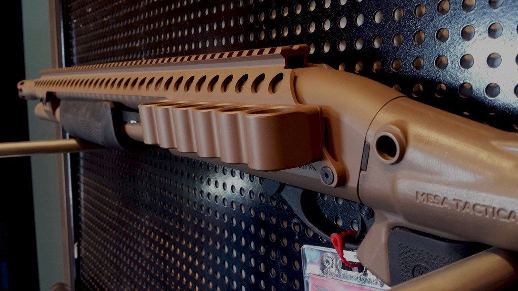 Tan shotgun with side shell holder on display.