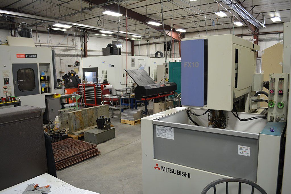 Workshop with various industrial machines, including a Mitsubishi EDM machine in the foreground.