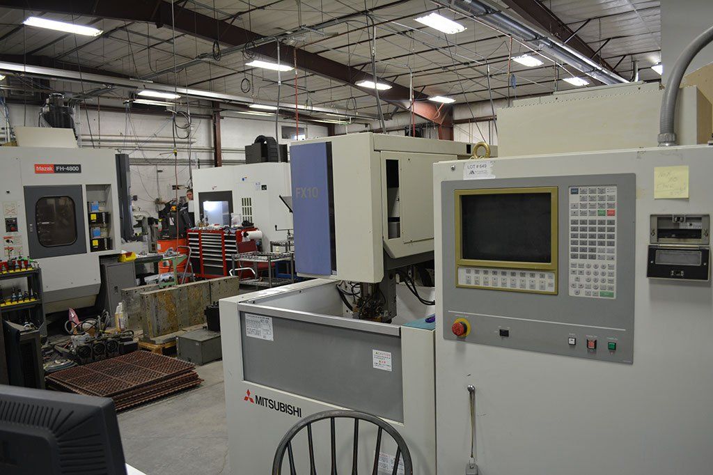 A manufacturing workshop with CNC machinery, including a Mitsubishi EDM and control panels.