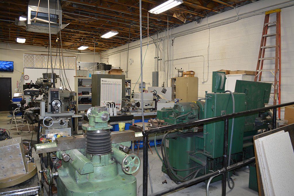 Workshop interior with machinery, tools, and a ladder against a wall.