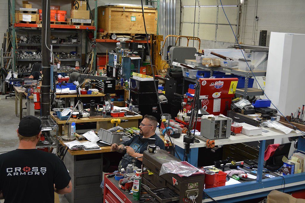 Workshop interior with two men working at cluttered workbenches; tools and equipment on shelves.