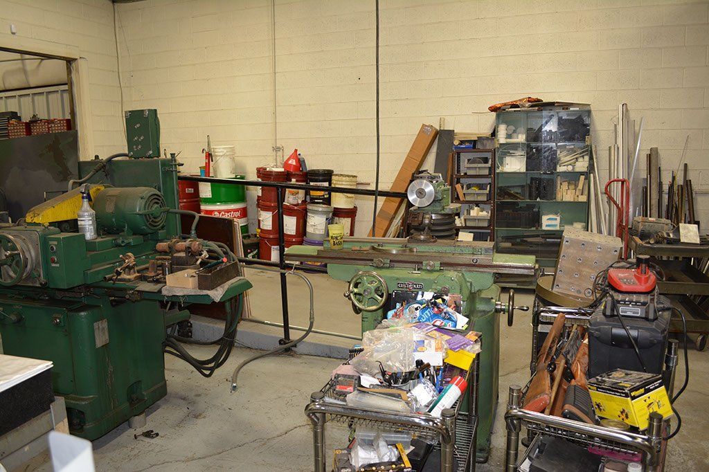 Workshop interior with industrial machinery, tools, and cluttered work surfaces.