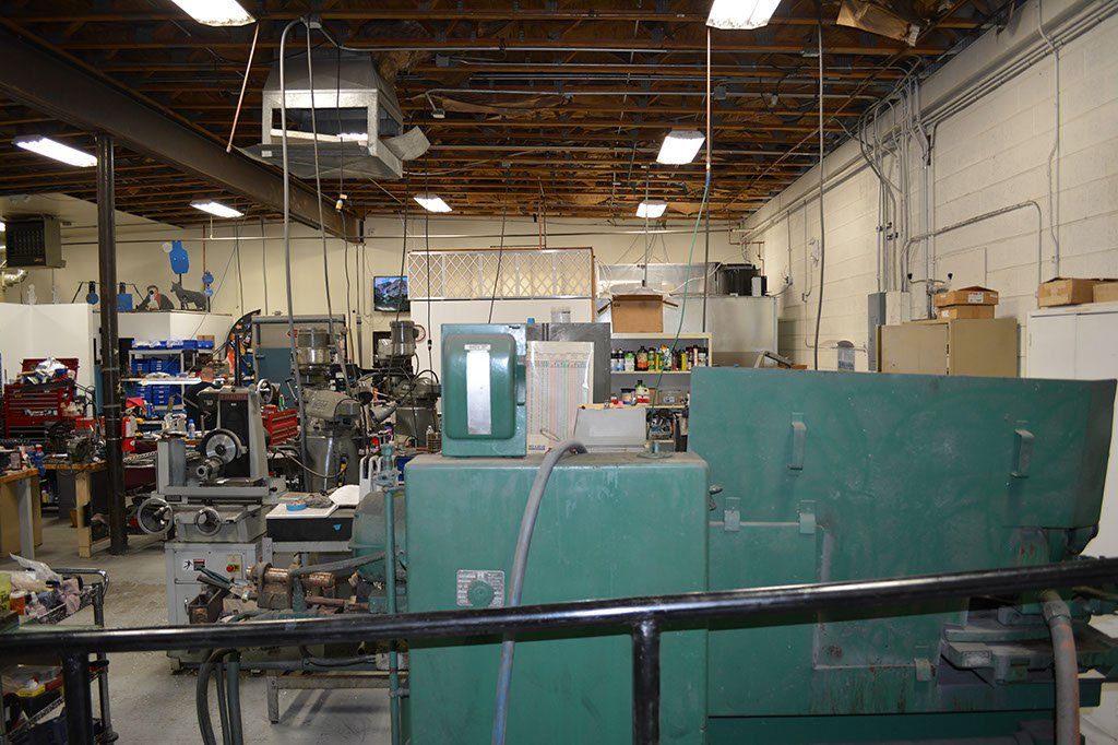 Green industrial machine in a cluttered workshop with exposed ceiling beams and various equipment.