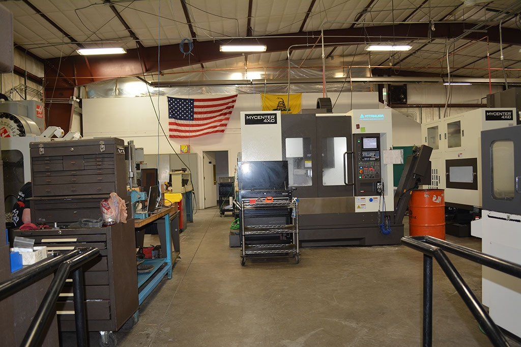 Machine shop interior with machinery, American flag, tools, and a person near the machinery.