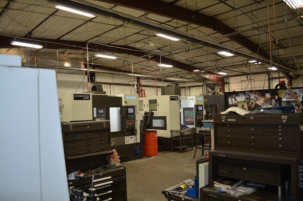 A workshop interior with multiple CNC machines, tool cabinets, and overhead lighting.