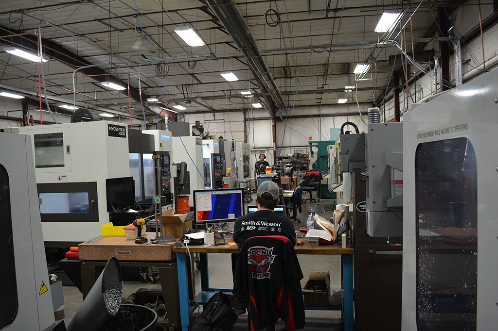 Inside a machine shop, a person works at a desk, surrounded by machinery.