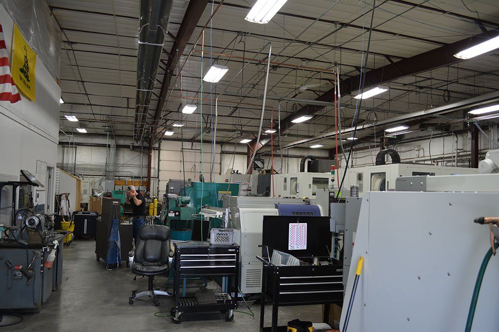 Inside of a manufacturing shop, machinery and tools, a person standing by a machine and looking at it.