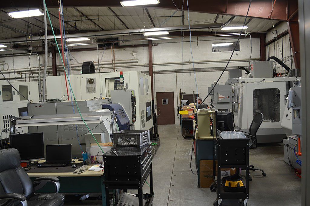 Interior view of a machine shop with multiple CNC machines, equipment, and a computer setup.
