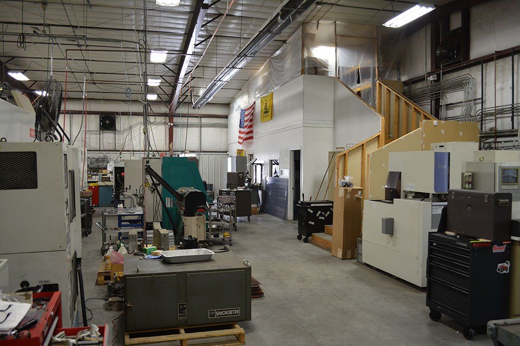 Interior of a manufacturing workshop with machinery and equipment. Staircase leads to a second level.
