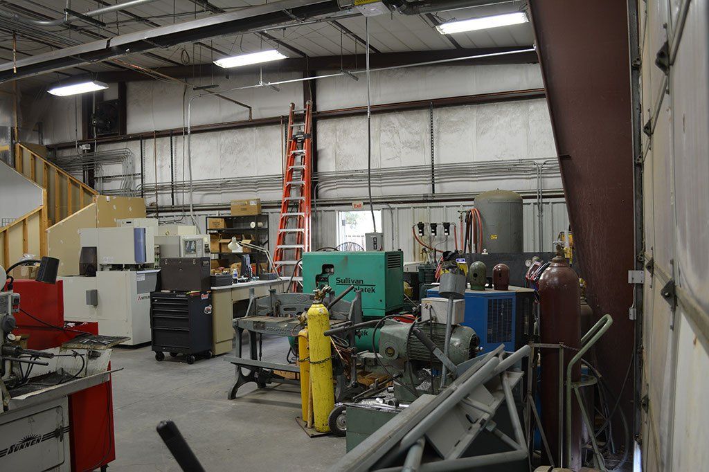 Workshop interior with tools, machinery, and a tall ladder. Green generator and red toolbox visible.