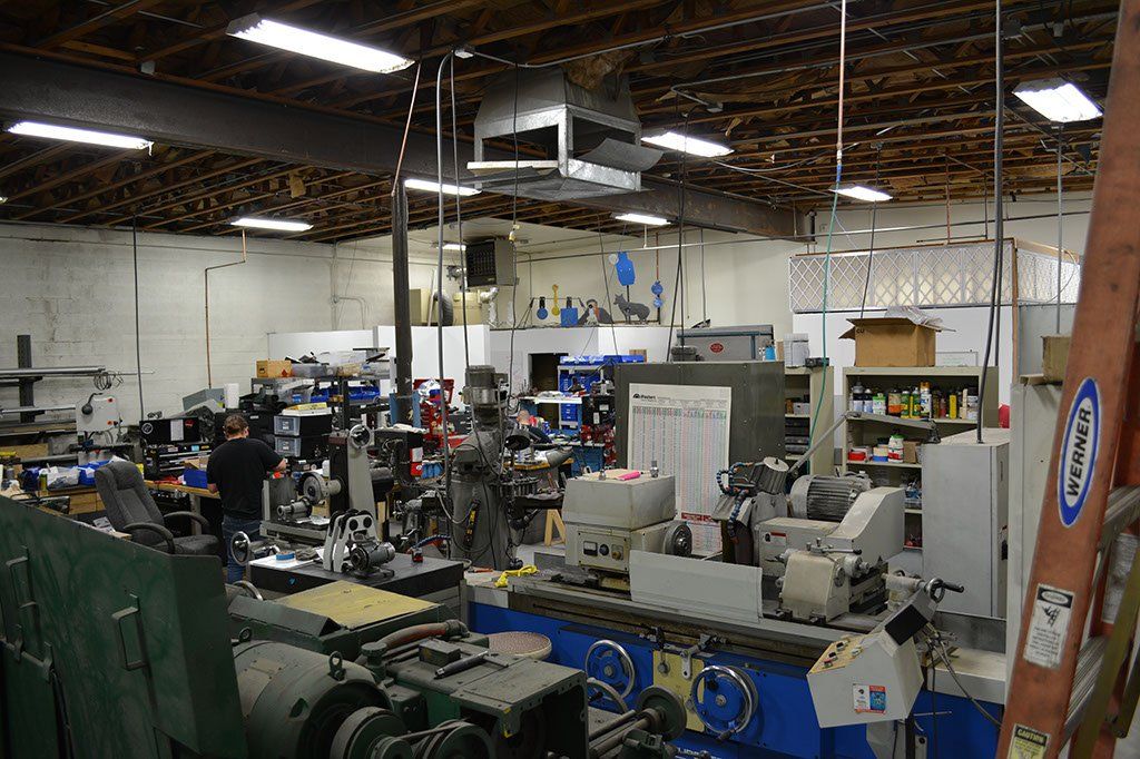 Machine shop interior with various equipment, tools, and a person working. High ceiling and cluttered environment.