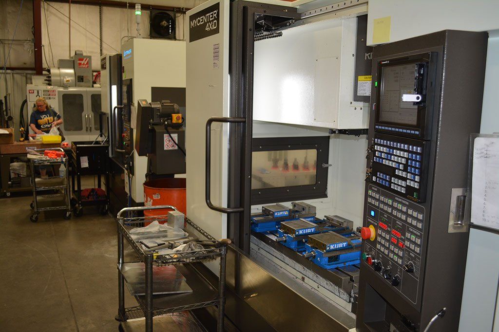 A CNC machine inside a manufacturing facility. It has a control panel, a work area with blue fixtures.