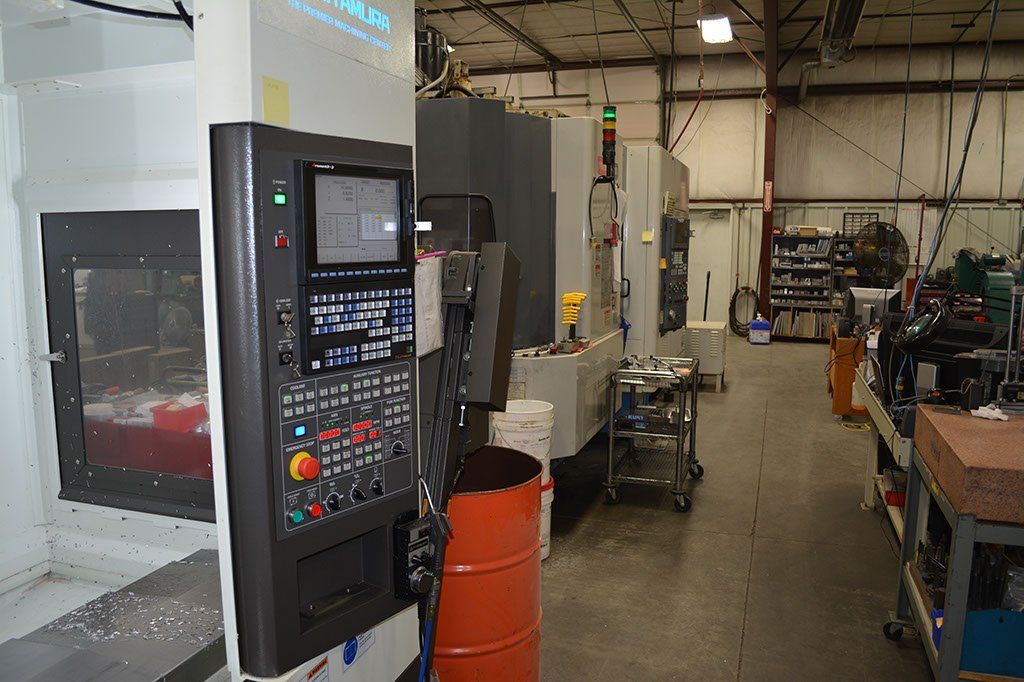 Control panel of a CNC machine in a workshop. Orange drum and other machinery in the background.