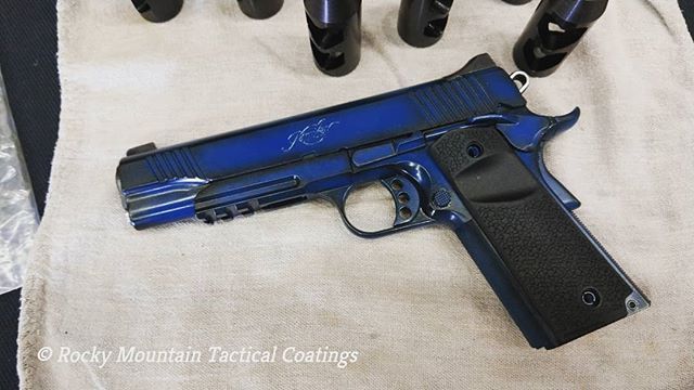 Blue and black custom handgun with signature on a cloth. Black barrel attachments in background.