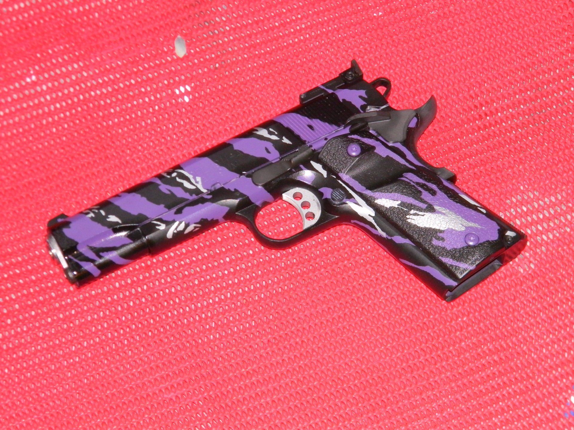 Purple and black camouflage handgun on a red surface.