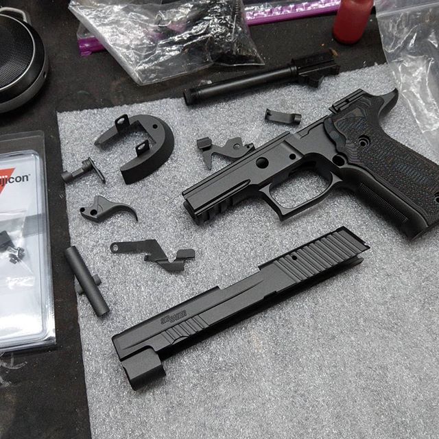 Disassembled handgun and parts on a gray surface, including the frame, slide, barrel, and trigger components.