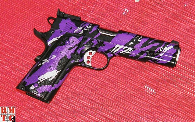 Purple and black camouflage pistol on a red surface.