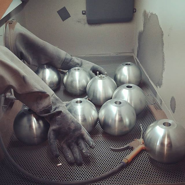 Hands wearing gloves arranging multiple metallic spheres inside a blast cabinet.