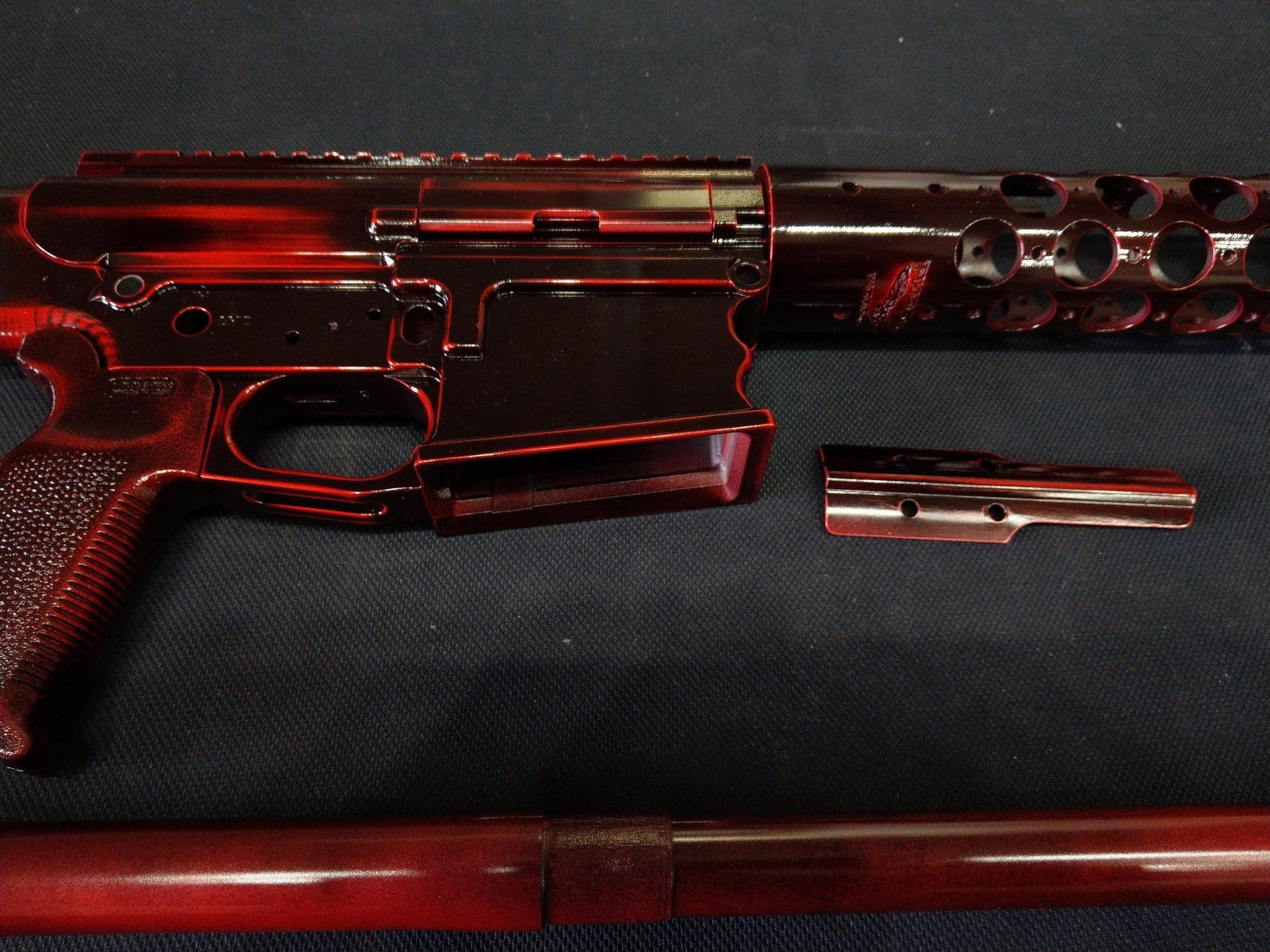 Red and black firearm parts laid out, featuring a rifle receiver, barrel, and other components.