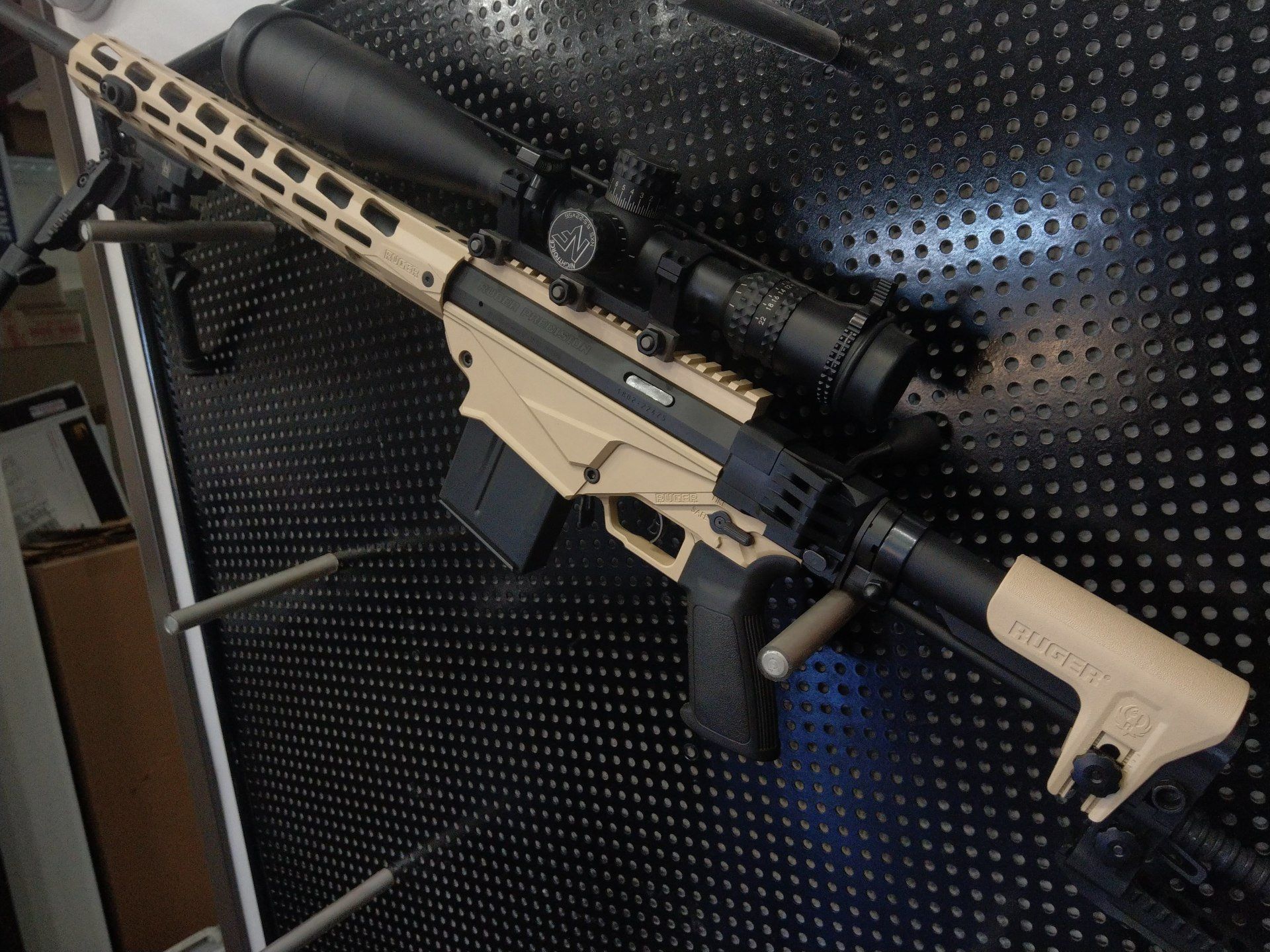 Tan and black rifle with scope and magazine on a textured surface.