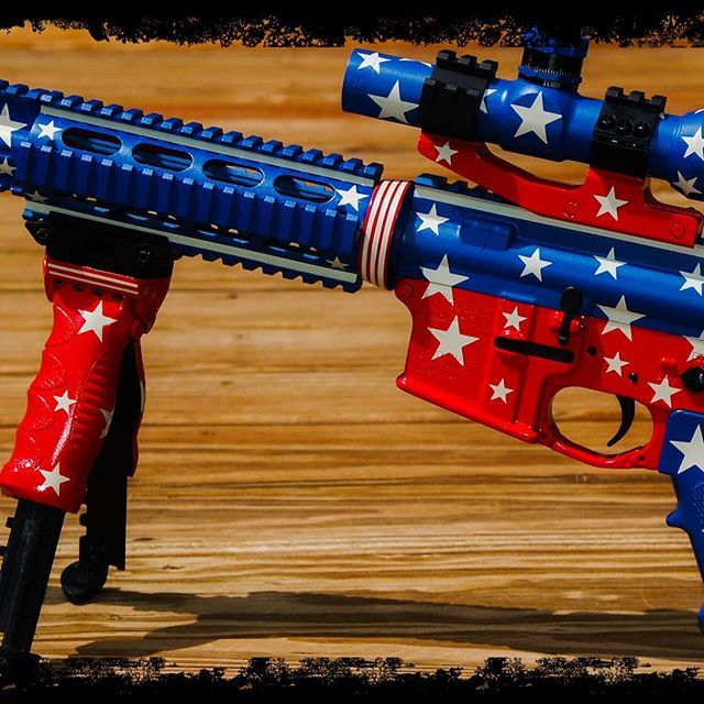 AR-15 rifle painted in red, white, and blue with stars, resting on a wooden surface.