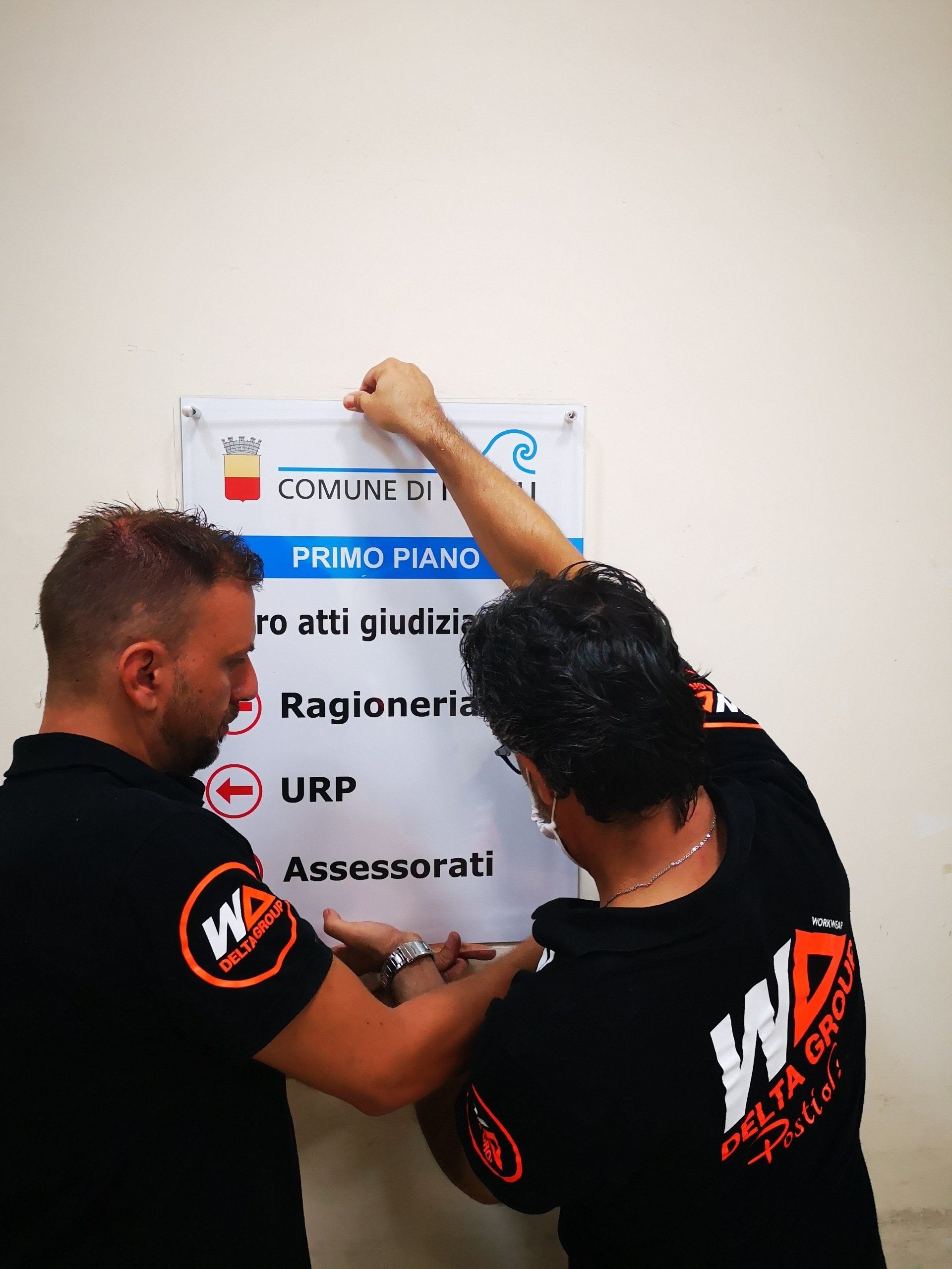 Due persone appendono un cartello a un muro, una delle quali utilizza una livella rossa.