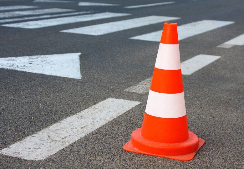 Cono stradale arancione su una strada con segnaletica orizzontale bianca e strisce pedonali.