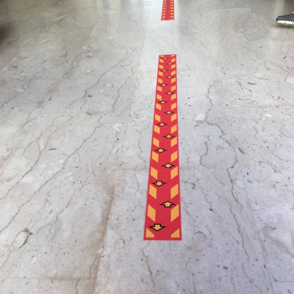 Segnaletica direzionale rossa su un pavimento di marmo in un corridoio.