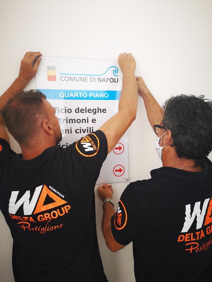 Two workers hang a “Comune di Napoli” sign on a wall.