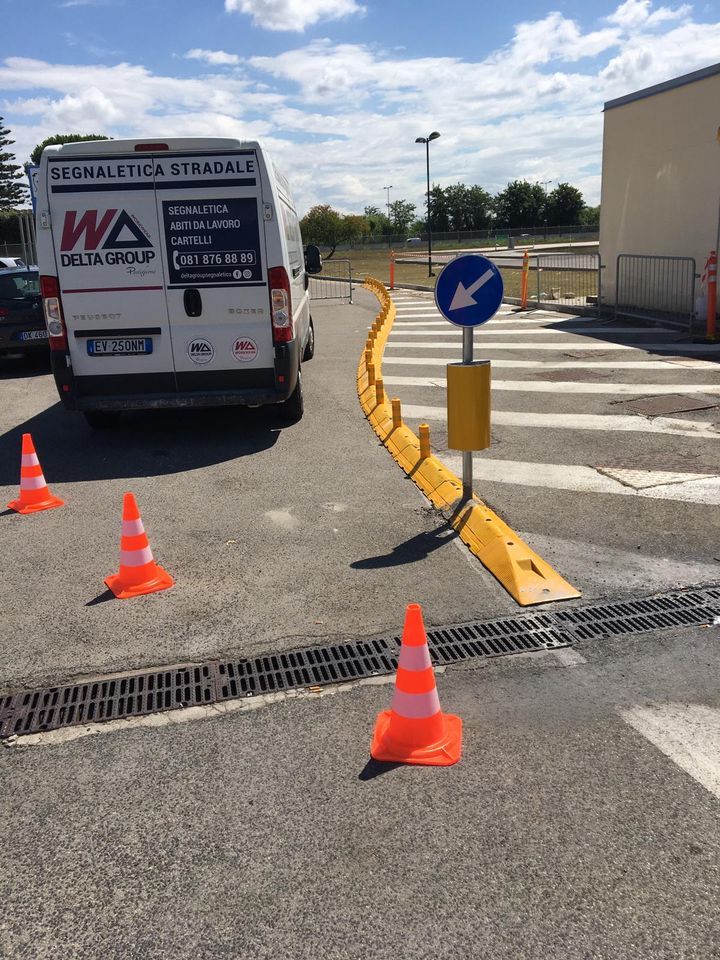 Barriera di traffico nel parcheggio con coni, cordolo giallo e segnale di senso unico accanto a un furgone.