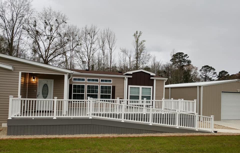 Exterior view of a ranch-style home with a wheelchair ramp. White railing, gray siding, brown accent, cloudy day.