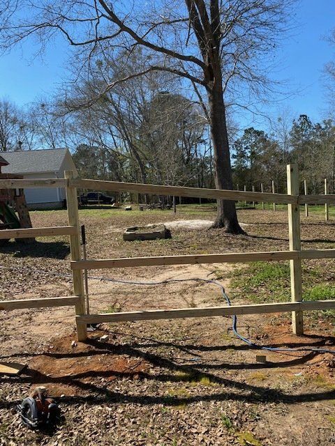 Wooden fence with gate in yard, tree in background, blue sky.