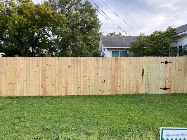 Wooden fence with gate, set in green yard. House and trees in background.